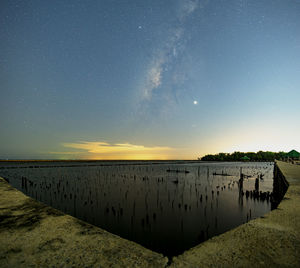 Wooden posts in lake against sky at night