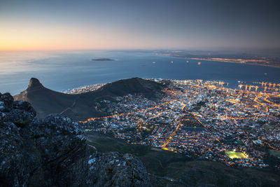 Aerial view of mountain and illuminated city by sea against sky at dusk