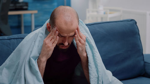 Young man having headache sitting on sofa