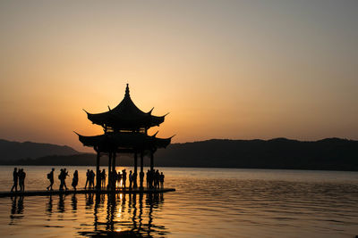 Silhouette people on lake against sky during sunset