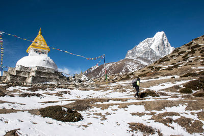 Woman walking by temple on mountain against sky during winter
