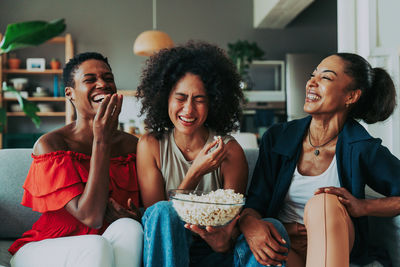 Smiling friends using smart phone while sitting at home