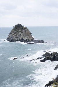 Rock formations at sea against cloudy sky