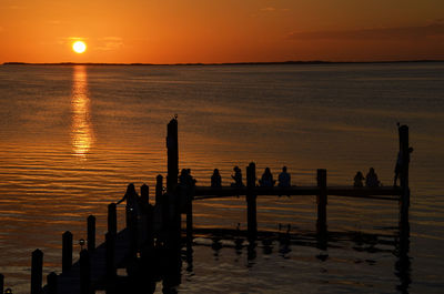 Silhouette of people sitting on pier in sea