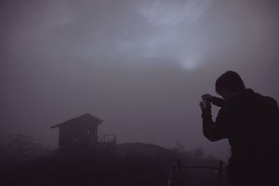 Silhouette man photographing against sky during foggy weather