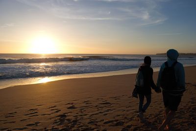 Friends walking on sand against sea during sunset