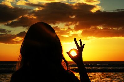Silhouette woman gesturing ok sign against sea during sunset