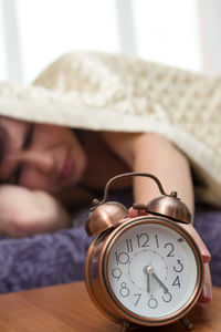 A sleepless woman reluctantly reaches out from under the blanket to the alarm clock.