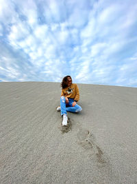 Full length of woman sitting on sand at beach against sky