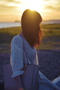 Rear view of woman against lake during sunset