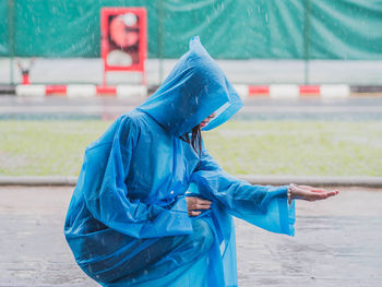 Side view of woman wearing blue raincoat catching rain