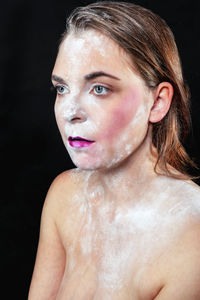Close-up of shirtless woman with make-up and talcum powder against black background
