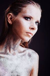 Close-up of young woman with silver bodypaint over black background