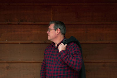 Mature man looking away while standing against wall