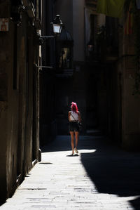 Rear view of woman walking on footpath amidst buildings in city