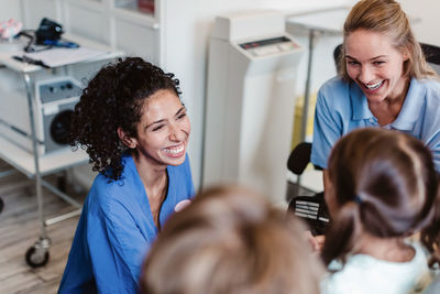 High angle view of smiling pediatrician and nurse talking with girl in medical examination room