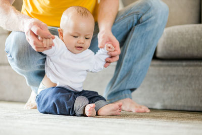 Low section of father and son sitting on floor at home