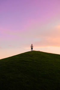 Rear view of man standing on field against sky during sunset