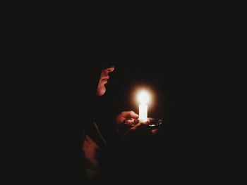 Close-up of person holding lit candle against black background