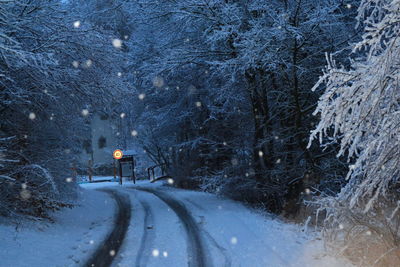 Road amidst snow covered trees against sky at night