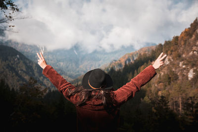 Rear view of young woman with outstretched arms in mountains, adventure.