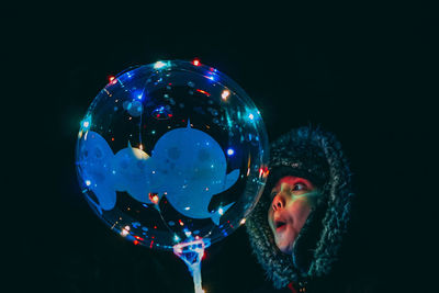 Portrait of woman holding bubbles over black background