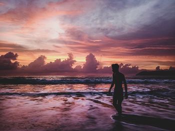 Silhouette man standing on beach against sky during sunset