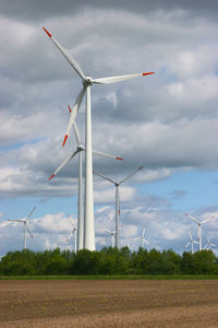 Wind turbines on field against cloudy sky