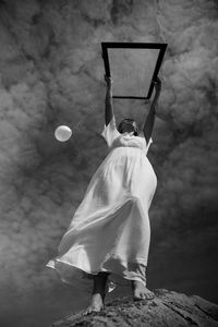 Low angle view of woman holding balloon with glass against sky