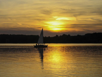 Silhouette sailboat in lake against sky during sunset