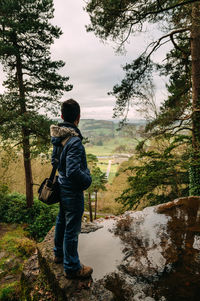 Rear view of man standing in forest against sky