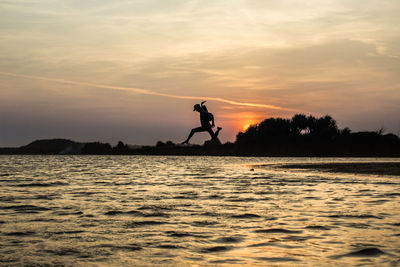 Silhouette man by sea against sky during sunset