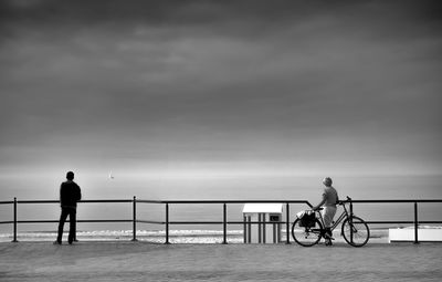 Bicycle standing on railing by sea against sky