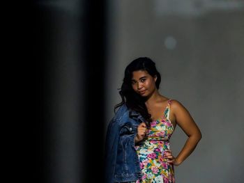 Portrait of beautiful woman holding denim jacket while standing against wall