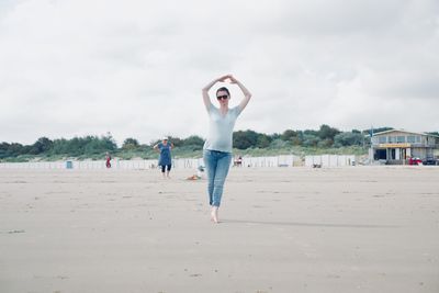 Full length of woman performing yoga at beach against sky