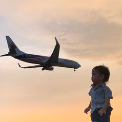 Side view of boy with airplane against sky during sunset