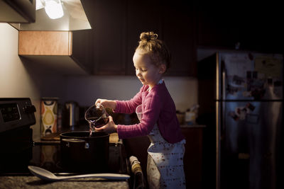 Side view of cute girl preparing food while standing in kitchen at home