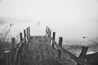 Wooden posts in sea against sky during winter