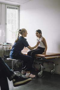 Female nurse examining girl sitting on bed in clinic