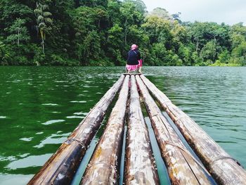 Rear view of woman sitting on bamboo boat in lake against trees