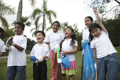 Happy friends holding equipment while standing against trees