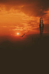 Silhouette bird flying against orange sky