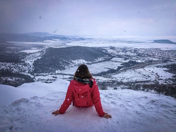 Woman with red jacket and backpack on top of the mountain in winter admiring the view