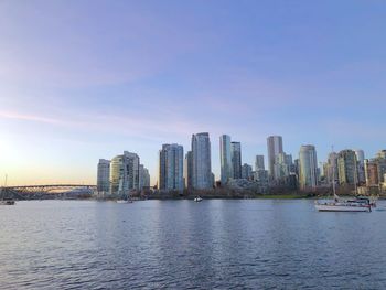 Sea by modern buildings against sky in city