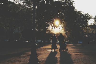 Rear view of silhouette man and woman with baby carriage walking on road