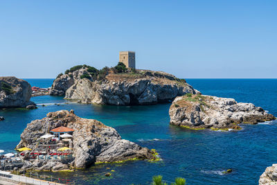 Rock formations by sea against clear blue sky