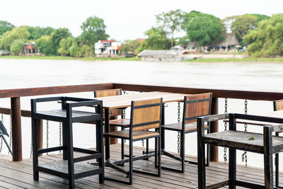 Empty chairs and table by river against trees