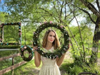 Portrait of young woman standing against trees