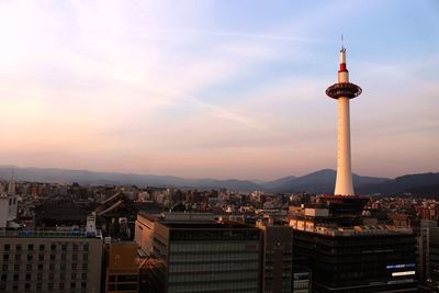 Communications tower in city against sky during sunset