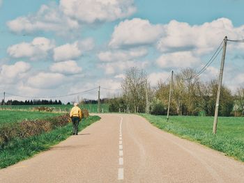 Rear view of man walking on road by field against sky